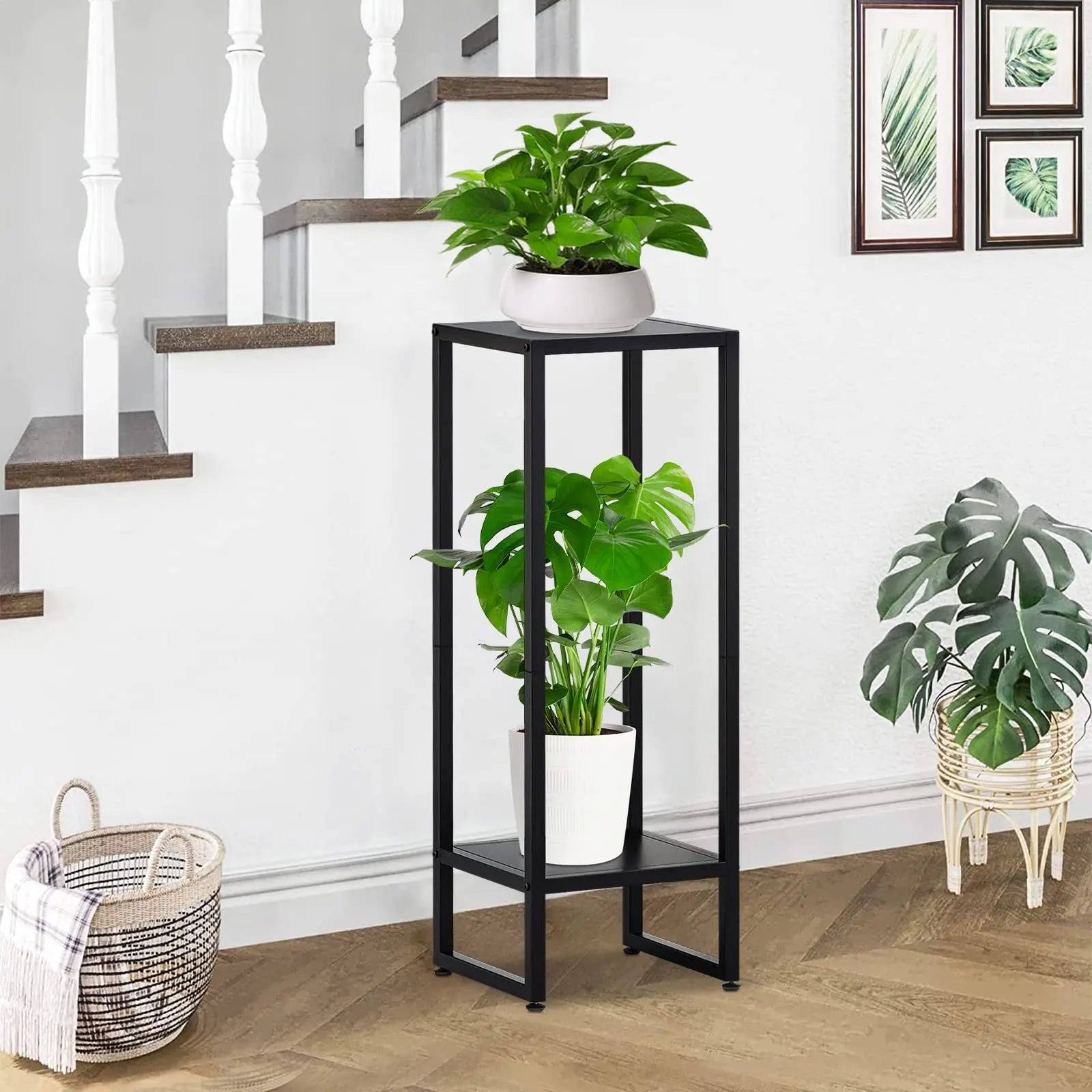 Black metal plant stand with two levels, holding green plants next to a staircase in a home interior.