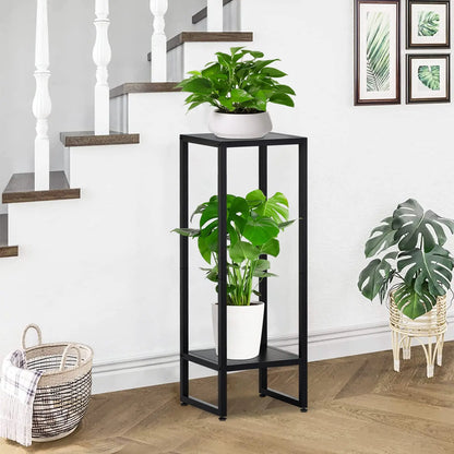 Black metal plant stand with two levels, holding green plants next to a staircase in a home interior.