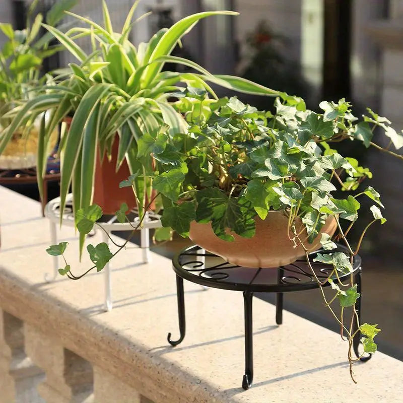 two metal plant stands placed outdoors on a stone ledge. Each stand is holding a potted plant.